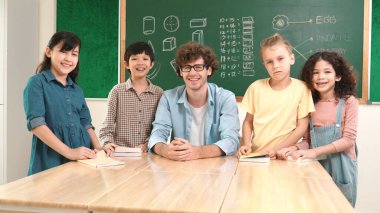 Profesyonel Kafkas öğretmeni ve çeşitli öğrenciler kameraya bakarken mutlu okul çocuğu gülümsüyor. Sınıfın önünde dururken gülümseyen bir grup çok kültürlü çocuk. Eğitim. Pedagoji.