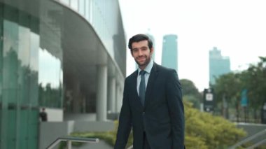 Profesyonel iş adamı hareket ediyor ve kameraya bakarken ayakta duruyor. Gülümseyen yönetici kameraya kendinden emin bir şekilde gülümsüyor. Mimari binada takım elbiseli yatırımcıların yakın çekimi. Sevinçli..