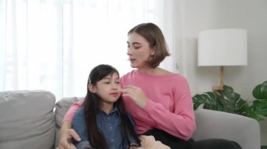 Kafkasyalı anne kızını kucaklıyor ve kanepede oturuyor ve alnından öpüyor. Mutlu anne oturma odasında sevimli Asyalı liseli kıza sevgi ve sevgi gösteriyor. Güzel bir aile birlikte vakit geçirir. Pedagoji.