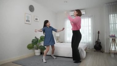 Yatak odasında Asyalı kızıyla müzik eşliğinde dans eden mutlu çekici anne. Beyaz anne dans eder ya da egzersiz yapar. Bu arada tatlı çocuk da müzik eşliğinde yatağa atlar. Aile eğlence konsepti. Pedagoji.