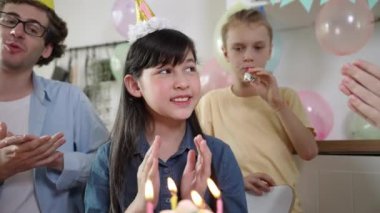 Mutlu şirin çocuk bir dilek diliyor ve doğum günü pastası mumu üflüyor. Özel bir kutlama için aile şapkası takıyor. Aile el çırparken kızların mum üfleme sahnesi. Pedagoji.