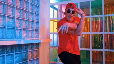Komik break dansçı kameraya bakarken hiphop 'a doğru serbest adım atıyor. Çılgın mutlu hipster dans edip sokak dansı yaparken Led ışığında günlük kıyafet ve güneş gözlüğü takıyor. Mutluluk.