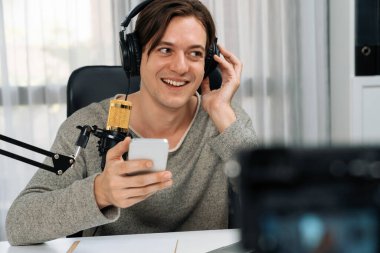 Akıllı yayıncının sunucu kanalı canlı sosyal medya yayını ile akıllı telefon kullanarak dinleyiciyle sohbet ediyor, kulaklık takarak modern ev stüdyosunda video kaydediyor. Bireysel.