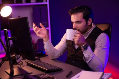 Gülümseyen zeki işadamı, elinde kahve fincanı olan satış ekibiyle buluşuyor ve geceleri Mor Neon Light Home Office 'deki bilgisayar ekranında ürün hedef pazarını araştırıyor. Tahmin et..