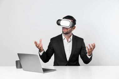 Profesyonel proje yöneticisi dizüstü bilgisayar başında otururken VR gözlüğü kullanıyor. Görsel gerçeklik kulaklığı takan yetenekli bir iş adamı metaevren ya da görsel dünyayı birbirine bağlıyor. Yenilik. Sapma.