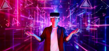 Afrikalı adam, VR kulaklık takıp parlak mavi ve pembe geometrik şekillerde dururken metaevreni keşfetmek için heyecanlanıyor. Oyuncu artırılmış gerçeklik gözlüğü kullanırken oyun oynuyor. Yaratıcılık.