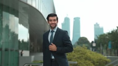 Profesyonel iş adamı hareket ediyor ve kameraya bakarken ayakta duruyor. Gülümseyen yönetici kameraya kendinden emin bir şekilde gülümsüyor. Mimari binada takım elbiseli yatırımcıların yakın çekimi. Sevinçli..