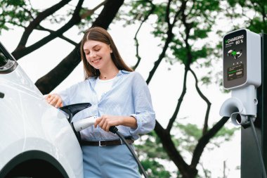Yolculuk sırasında doğal orman ya da milli parktaki elektrikli araba için şarj olan genç bir kadın. Tatil ve tatil boyunca çevre dostu seyahat. Yükselt