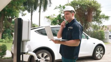Evde EV şarj istasyonu kurulumu üzerinde çalışan nitelikli teknisyen, EV için dizüstü bilgisayarla şarj sisteminde sorun çıkarma ve yapılandırma ayarları yapıyor. Titiz