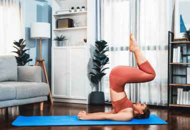 Spor kıyafetleri içinde esnek ve becerikli bir kadın evde egzersiz paspası üzerinde meditasyon pozisyonunda yoga yapıyor. Huzurlu ve huzurlu bir yoga yaşam tarzı..