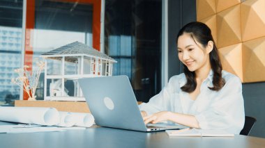 Genç ve güzel mimar mühendisin portresi çatı malzemelerini kontrol ediyor ve ofisteki masaya yerleştirilmiş proje planı ve ev modeliyle dizüstü bilgisayar kullanıyor. Yaratıcı iş tasarımı konsepti. Yönlendirici.