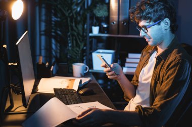 Genç işadamı e-posta aramak için akıllı telefonu kullanıyor. Neon Modern Ofis 'teki yaratıcı proje çalışma masasını kontrol etmek için elinde evrak tutmakta olan müşteri ya da iş arkadaşıyla sohbet ediyor. Toplayıcı.