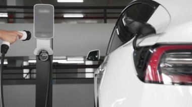 Yavaş çekim kadın, EV elektrikli arabasıyla şehir merkezindeki alışveriş merkezinin otoparkına gidiyor. Sürdürülebilirlik yaşam tarzını yeşil, temiz, yeniden şarj edilebilir elektrikli araç iç organlarıyla şarj ediyor.