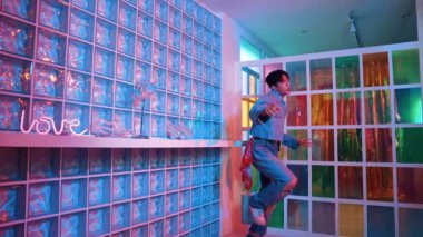 Çekici Asyalı sanatçı parlak neon ışıkta adım atıyor. Kameraya özgüvenle bakarken serbest stil müzikle dans eden yakışıklı break dans. Profesyonel hippi rahatla. Mutluluk.