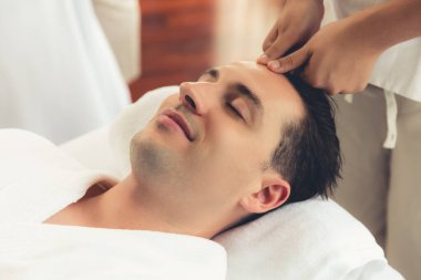 Beyaz adam stres önleyici kafa masajından ve lüks bir tatil beldesi veya otel spa salonundaki modern ışık ortamında yüz güzelliği eğlencelerini şımartmaktan hoşlanıyor. Sessiz.