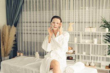 Kaplıca salonunun sakin, modern gün ışığı atmosferi, kadın müşteri poz veriyor ve yüz maskesi ile gençleştiriyor. Yüz bakımı ve güzellik kozmetolojisi prosedürü. Sessiz.