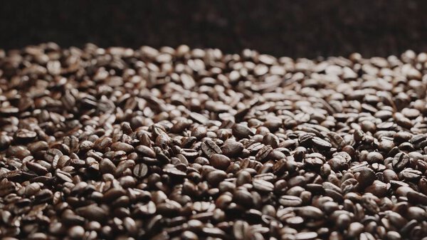 Macro shot of super slow motion shot of fresh coffee bean placed with black background. Close up of piles of aromatic roasted coffee seed surrounded. Macrography. Beans scattering around. Comestible.