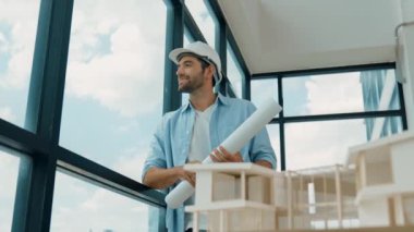 Gökdelen manzarasına bakarken yürüyen profesyonel mimar mühendisi. Masaya yerleştirilmiş ev modeliyle pencereye bakarken yetenekli proje yöneticisi proje planını tutuyor. Tasarım. İzleme