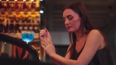 Oturan güzel bir bayan misafir, arkadaşlarıyla beklemekten sıkılıyor ya da Bokeh gece kulübünde lüks bir tezgah barda mavi Hawaii kokteylinde karışık votka içmekten sıkılıyor. Vinosity.