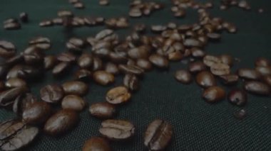 Karışık aromalı kahve çekirdeği yığını masaya saçılmış ve kavrulmuş kahve çekirdekleri etrafa saçılmış siyah arkaplanla çevrilmiş. Makrografi. Ağır çekim. Pabulum.