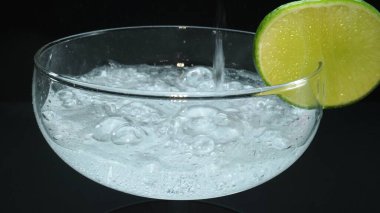 Bir margaritanın makrografisi bir bardağa dolduruluyor canlı bir limon dilimiyle süsleniyor, hepsi siyah arka plana karşı. Her yakın çekim kokteyl ve taze limonun detaylarını yakalar. Geliştirilebilir.