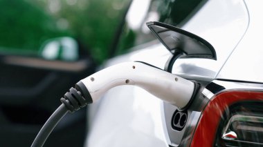 Doğal yeşil şehir parkındaki otoparkta EV elektrikli araba şarj pili. Sürdürülebilir ve çevre dostu seyahat için yenilenebilir otomobil için alternatif temiz enerji teknolojisi. Eşzamanlama