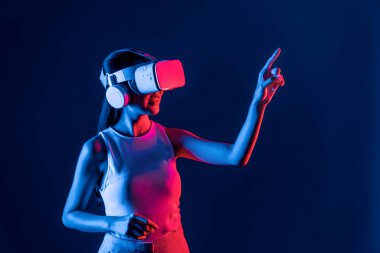 Siberpunk neon ışıklı cihazlarla çevrili zeki bir kadın metaevrene bağlı VR kulaklık takıyor, gelecekçi siber uzay teknolojisi. Sanal objeyi işaret eden bir kadın. Halüsinasyon.