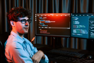 Ekranda yazılım geliştirme bilgisine karşı oturan gülümseyen bilişim geliştiricisinin profili, web sitesindeki son sürüm uygulaması için program kodlaması oluşturarak çevrili kameraya bakıyor. Toplayıcı.