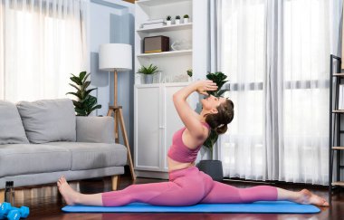 Spor kıyafetleri içinde esnek ve becerikli bir kadın evde egzersiz paspası üzerinde meditasyon pozisyonunda yoga yapıyor. Huzurlu ve huzurlu bir yoga yaşam tarzı..