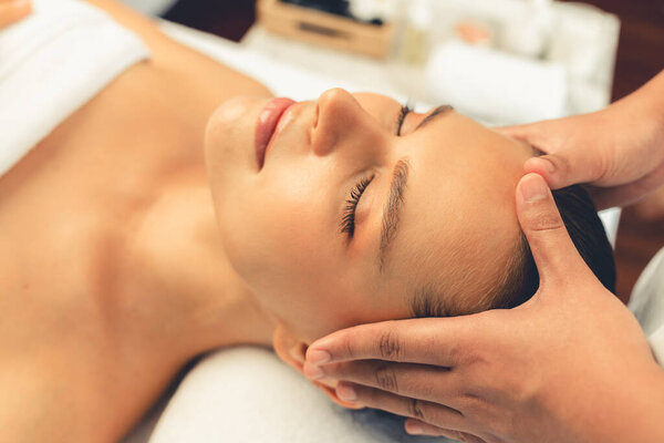 Кавказская женщина наслаждается расслабляющим антистрессовым массажем головы и расслабляющим отдыхом на коже лица в дневном спа-салоне современного света в роскошном курорте или спа-салоне отеля. Quiescent