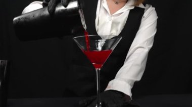 Makrografi, bir barmenin martini bardağına canlı kırmızı bir kokteyl karıştırma sanatına tanık olmak, güzel süslenmiş taze bir biberiye ve parlak siyah bir arka plan. Geliştirilebilir.