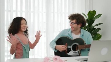 Çekici beyaz bir baba gitar çalarken tatlı bir kız müzik eşliğinde dans ediyor. Mutlu baba ve Amerikalı kız birlikte vakit geçirirken akıllı çocuk müzik yapıyor. Aile eğlence konsepti. Pedagoji.