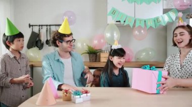 Çekici beyaz kız, ebeveynleri kutlama yaparken ve parti şapkası takarken doğum günü hediyesi alıyor. Mutlu genç çocuk gülümserken mutlu aile özel günü kutlamak için el çırpıyor. Pedagoji