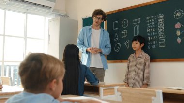 Öğrenci sınıfın önünde duruyor ve beyaz bir öğretmen öğrenciye bakıp çocuğu cesaretlendirirken kendini sınıfa tanıtmaya başlıyor. Çeşitli çocuklar oturur ve oğlanlara bakarlar. Pedagoji.