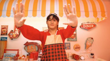 Profesyonel Asyalı restoran işçisi dans ediyor ve yemek barının arkasında duruyor. Kırmızı tişörtlü ve kırmızı önlüklü çekici garson kameraya bakarken serbest stil müziğe yöneliyor. Çılgın dans. Mutluluk.