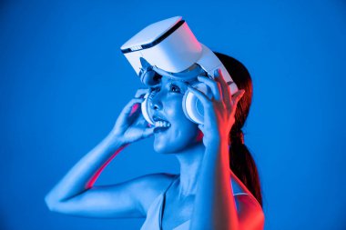 Zeki bir kadın gözünün üzerine VR bağlayan neon ışığı kulaklığı ile ayakta duruyor. Meta-evreni, gelecekteki siber uzay teknolojisini bağlayan cihaz. Elle gözlük tutan bir kadın. Halüsinasyon.