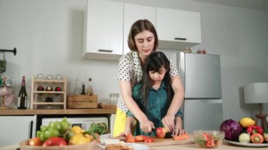 Zeki beyaz anne ve Asyalı kız birlikte yemek pişiriyor ve sebze doğruyor ya da akşam yemeği için salata hazırlıyor. Mutlu anne ve kız taze yemekle sağlıklı yemek yapıyorlar. Sağlıklı gıda konsepti. Pedagoji.