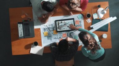 İnşaat mühendislerinin masa başında proje planıyla otururken tablet kullanarak ev yapısını dizayn etmelerine tepeden aşağı bir bakış açısı. Ekip planlama ve inşaat hakkındaki fikirlerin havadan görüşü. Sempozyum.