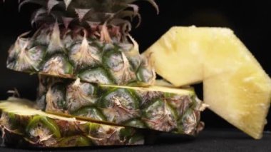 Taze ananaslı ve ayrı siyah arkaplanlı bir ananas dilimli videoyu kapat. Kaba ve balmumu kabuğu, dikenli yeşil yapraklardan bir taç, yemek fotoğrafçılığı. Geliştirilebilir.