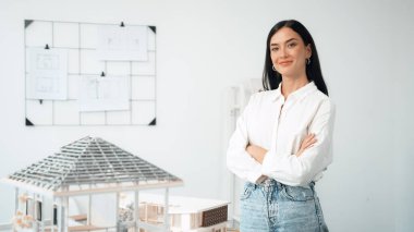 Genç, güzel, profesyonel mimar mühendisin portresini yakın plan ile birlikte beyaz modern ofiste ev modeliyle güven içinde pozlar veriyor. Yaratıcı yaşam ve tasarım. Tertemiz..