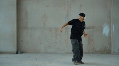 Kulaklıktan çimento arka planda müzik dinlerken break dans pratiği yapan yakışıklı bir hippi. Sokak dansçısının hareketli çekimi robot dansı yapar. Açık hava sporu 2024. Modern dans. hiphop.