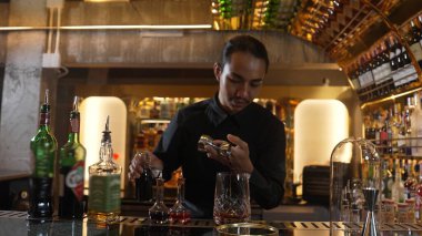 Güzel görünümlü Asyalı barmen içki şurubunu kullanarak lüks içki tezgahında cam hazırlama, gece kulübü lüksündeki düzgün profesyonel barmen kostümü yapıyor. Vinosity.