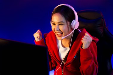 Yüzünde kulaklık renginde kulaklık takan, neon odada online oyun oynayan, Esport meziyetli takım oyuncularına yumruk kaldırarak oynayan güzel Asyalı kız flamasının sunucu kanalı. Taktik.