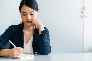 Güzel genç Asyalı kadın ofis masasında otururken deftere mektup yazıyor. İçerik yazarı ve sekreter iş konsepti. uds