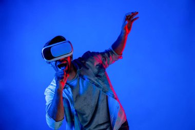 Sanal programı keşfetmek ve girmek için VR gözlük takan heyecanlı bir adam. Yetenekli oyuncular metaevrene dokunurken gündelik giysiler giyer ve neon ışıklı arka planda dururlar. Yaşam tarzı. Sapma.