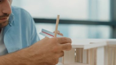 Akıllı inşaat mühendisinin el ölçümü ev modeli inşaatı. Gündelik kıyafetlerle profesyonel mimar bina inşaatı planlarken ev modeline bakıyor. Eline odaklan. İzleme