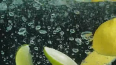 Bir bardak temiz suya düşen taze limon ve limon dilimlerini kapatın. Sarı limonlu makro dökülüyor ve koyu arkaplanlı suya dökülüyor. Makrografi. C vitamini Pabulum..