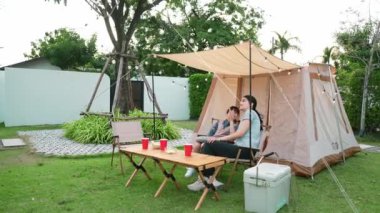 Aile hep birlikte bahçedeki kampta oturup yemek yiyor. Ebeveynler, genç nesil arasında iletişim kurmak ve zaman geçirmek için açık hava kamp faaliyetlerini kullanıyorlar. Uyumsuzluk.