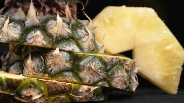 Taze ananaslı ve ayrı siyah arkaplanlı bir ananas dilimli videoyu kapat. Kaba ve balmumu kabuğu, dikenli yeşil yapraklardan bir taç, yemek fotoğrafçılığı. Geliştirilebilir.