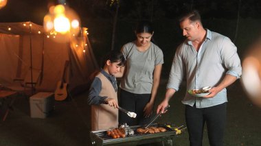 Aile tatilini bahçede kutlar. Baba, anne ve çocuk üyeleri için ızgara yapıyor. Açık hava kampı aktivitesi yemeğin yanında dinlenmek ve kuşaklar arası genç kuşaklarla zaman geçirmek için. Uyumsuzluk.